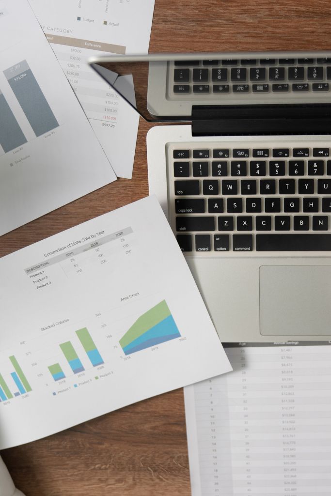 A laptop open next to paper charts and graphs, symbolizing the integration of IT solutions in accounting tasks.
