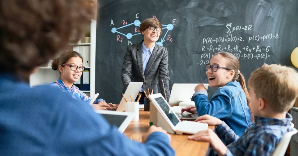 Teacher and students smiling and working together with tablets in a tech-integrated classroom, using IT GOAT’s tools to enhance collaboration and interactive learning.